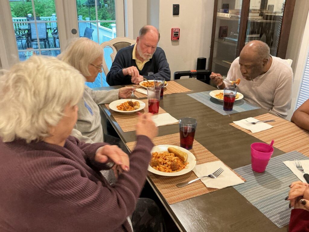 Residents and staff sharing a pasta meal together around the dining table