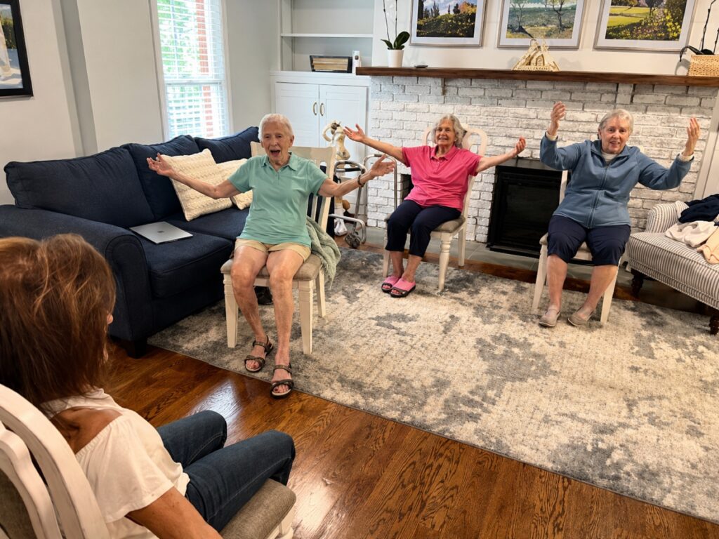 Three residents taking part in a seated chair-exercise class led by an instructor