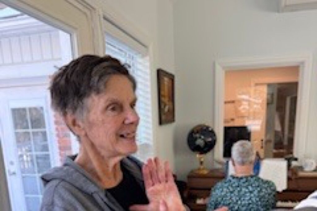 Resident standing in a sunlit sitting room, gesturing while talking with others
