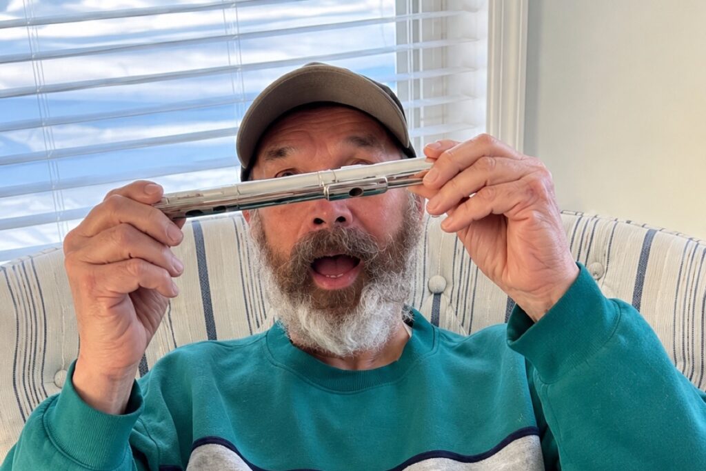 Smiling resident in a baseball cap holding a small wooden flute up to his face